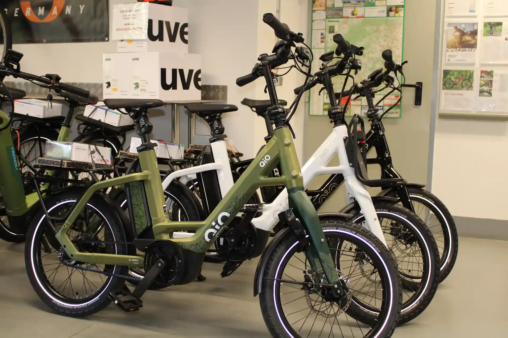 Kompakte E-Bikes von QiO bei AuFa vor dem Regal mit Uvex-Helmen